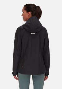 Schwarze Outdoor-Jacke mit Kapuze, mit strukturiertem Finish, verstellbaren Manschetten, Logo auf dem Rücken und subtilen orangen Akzenten am Saum.
