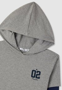 Felpa grigia in cotone con tasca frontale, un grande "02" in blu scuro e "Manhattan" in un font corsivo, con una manica in contrasto di colore blu navy.