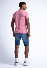 Camiseta de manga corta en tono rosa jaspeado combinada con pantalones cortos de mezclilla azul y zapatillas blancas. Costuras visibles y diseño de corte relajado.