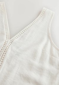 White sleeveless top with textured fabric and decorative openwork trim along the neckline and armholes.