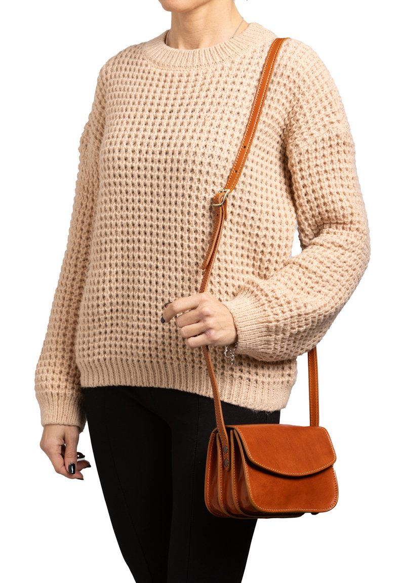 Maglione lavorato a maglia color beige con un motivo testurizzato, abbinato a una piccola borsa a tracolla in pelle arancione con chiusura a patta e tracolla regolabile.