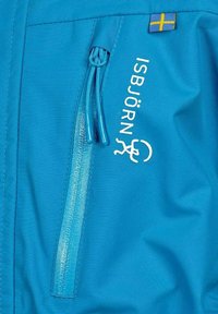 Blå jacktyg med vertikalt blixtlåsfack, vitt ISBJÖRN-logotyp och liten svensk flaggtagg nära axelsömmen.