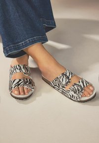 Platform sandaler med zebra print design, hvid bund, to spænder og en struktureret sål, placeret mod denim stof.