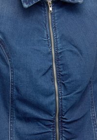 Denim jacket featuring a zip closure and gathered texture. Dark blue fabric with visible stitching details along the sides and collar.