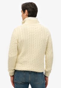 Crème kabelgebreide trui met hoge kraag, gestructureerd patroon en geribbelde manchetten. Draag met blauwe jeans voor een casual look.