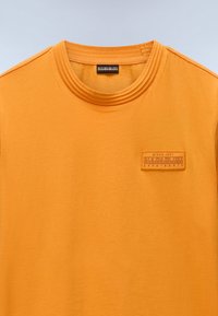 Oranje katoenen t-shirt met een geribde halslijn en een textuur logo patch aan de voorkant. Soepele textuur met een ontspannen pasvorm.