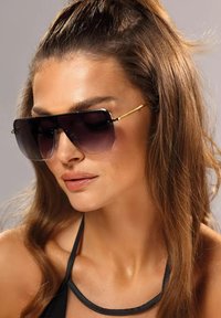 Okulary przeciwsłoneczne z przerośniętymi, ciemnymi gradientowymi soczewkami, czarnymi oprawkami i złotymi akcentami. Projekt charakteryzuje się smukłym, kanciastym kształtem.