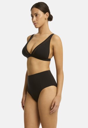 Modella in posa di profilo indossa un bikini nero composto da un top triangolare e uno slip a vita alta, che mette in mostra un design elegante e minimalista.