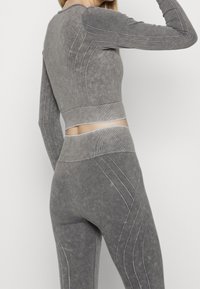 Grå atletisk set med en figursydd långärmad topp och högmidjade leggings, med texturerat tyg och kontrasterande sömmar.