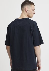 Námořnická modrá krátká rukávová tričko vyrobené z bavlny, s kulatým výstřihem a malým logem na zadním výstřihu. Hladká textura.