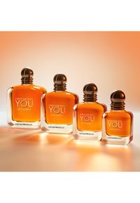 Firebunnede parfymeflasker i amberglass med avrundede brune lokk, med hvit tekst: "STYRKERE MED DEG INTENS." Ulike størrelser arrangert på rad.