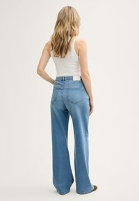 Svijetloplave hlače širokih nogavica s visokim strukom, koje imaju stražnje džepove i malu oznaku na pojasu. Glatka denim tekstura.