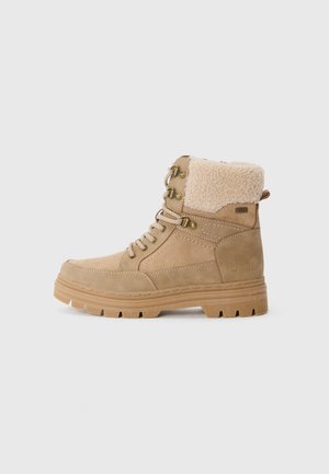 Bottines tan avec une tige en daim, doublure en fourrure, œillets en métal et semelle en caoutchouc texturée. Présente un design à lacets et un col rembourré.
