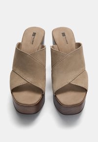Beige ruskinds-platform mules med kryds-stroppedesign, åben tå og en tekstureret brun træbund. Minimal branding på indersålen.