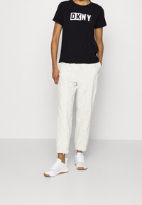 Czarny bawełniany T-shirt z logo "DKNY", zestawiony z białymi lekkimi spodniami i białymi trampkami z pomarańczowymi akcentami. Prosty design i swobodne dopasowanie.