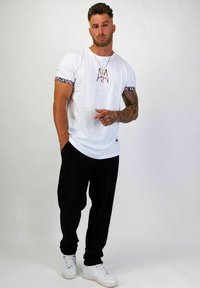 Vit T-shirt med färgglada mönstrade korta ärmar, med en central logotyp. Matchad med svarta byxor och vita sneakers.