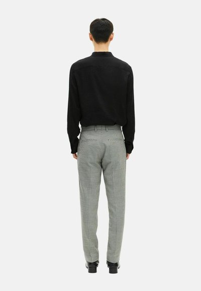 Una camicia nera a maniche lunghe e pantaloni grigi a quadri, con una vestibilità su misura e una lieve texture, mostrati da dietro. Scarpe nere completano l'outfit.