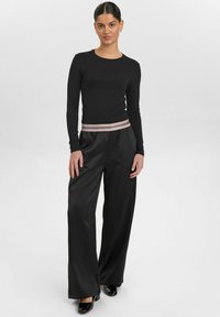 Zwarte lange mouwen top met ronde hals, gecombineerd met wijde zwarte satijnen broek met een roze en zilveren gestreepte tailleband.