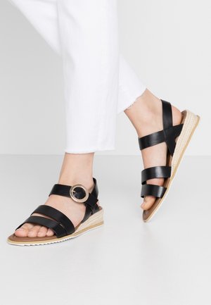 Czarne skórzane sandały z klamrą na koturnie, zaprojektowane z trzema paskami i okrąłym zapięciem. Podeszwa ma teksturowane wykończenie.