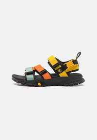 Sandalia negra con correas ajustables en naranja, amarillo y verde menta. Suela de goma gruesa con textura para mayor agarre. Diseño robusto.