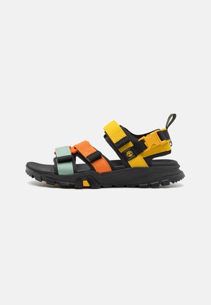 Sandalia negra con correas ajustables en naranja, amarillo y verde menta. Suela de goma gruesa con textura para mayor agarre. Diseño robusto.