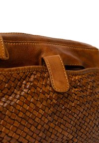 Primo piano di una borsa in pelle intrecciata marrone con patta in pelle cucita e zip visibile sotto la patta.