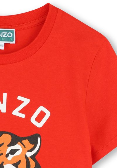 T-shirt en coton rouge présentant un graphique de tigre et le texte blanc "KENZO" sur le haut de la poitrine. Col rond avec une texture douce.