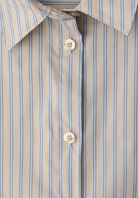 Beżowa koszula zapinana na guziki z niebieskimi pionowymi paskami, wyposażona w spiczasty kołnierzyk i dwa białe guziki. Gładka tekstura tkaniny.