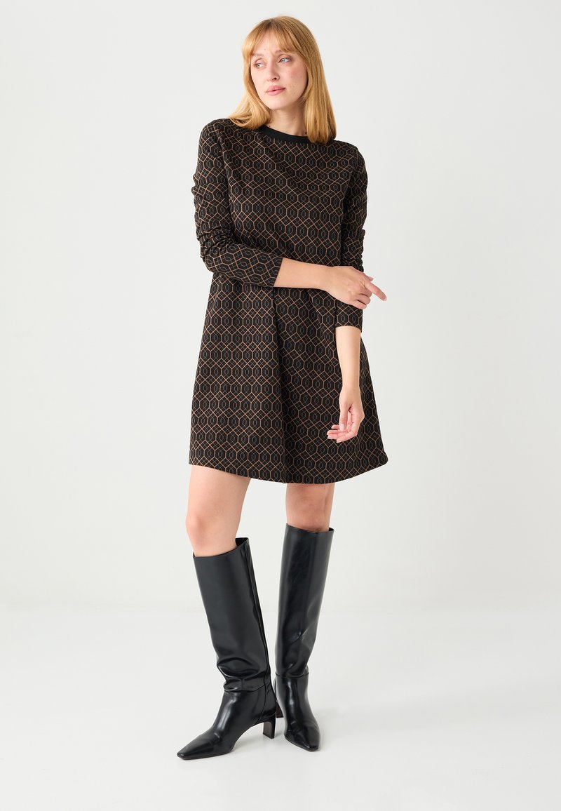 Robe noire à manches courtes avec un motif géométrique marron, jupe évasée et encolure ronde, associée à des bottes en cuir noires montant jusqu'au genou.