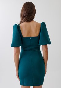 Teal dress with textured fabric, square back neckline, puff sleeves, zip closure, and fitted silhouette, hitting above mid-thigh.