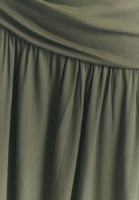 Abito di tessuto verde oliva con pieghe arricciate nella gonna, caratterizzato da una consistenza morbida e liscia e un design del corpetto drappeggiato.