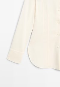 Cream-colored long-sleeve button-up shirt with a smooth texture, curved hem, and classic button details on cuffs and front placket.