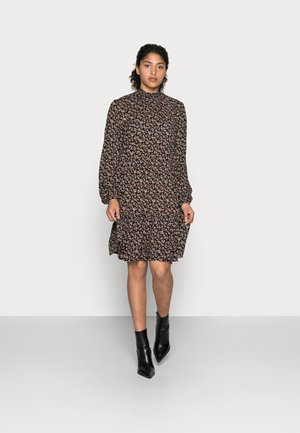 Schwarzes Blumenkleid mit langen Ärmeln, hohem Kragen und schichtweise gestuftem Rock. Das Muster zeigt kleine rosa und cremefarbene Blumen. Getragen mit schwarzen Chelsea-Boots.