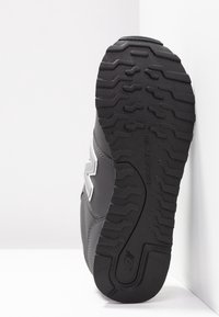 Semelle de basket New Balance noire avec motif de bande de roulement texturé, coutures visibles et partie du panneau latéral supérieur gris et blanc.