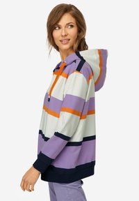 Felpa a righe viola e bianche con dettagli arancioni e blu navy. Presenta un cappuccio con coulisse, vestibilità ampia e maniche lunghe con polsini a coste.