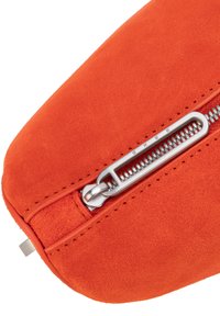 Oranžna semišasta torbica s srebrnim zadrgo. Ima gladko teksturo in poševno obliko. Poteg zadrge ima vgraviran zaščitni znak.