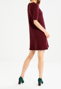 Burgundy texturerad klänning med korta ärmar och lös passform, kombinerad med gröna blockklackade skor. Klänningen slutar ovanför knät.