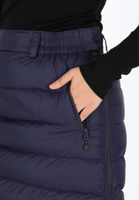 Laivastonsininen puskahame, jossa on vaakasaumat, joustava vyötärö ja vetoketjullinen sivutasku. Kangas vaikuttaa sileältä ja eristetyltä.