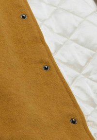 Brown wool fabric with three metal snap buttons lying next to a white quilted fabric surface.