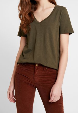 Olivgrünes Baumwoll-T-Shirt mit V-Ausschnitt und kurzen Ärmeln, kombiniert mit rostfarbenen Cordhosen mit strukturierter Oberfläche.