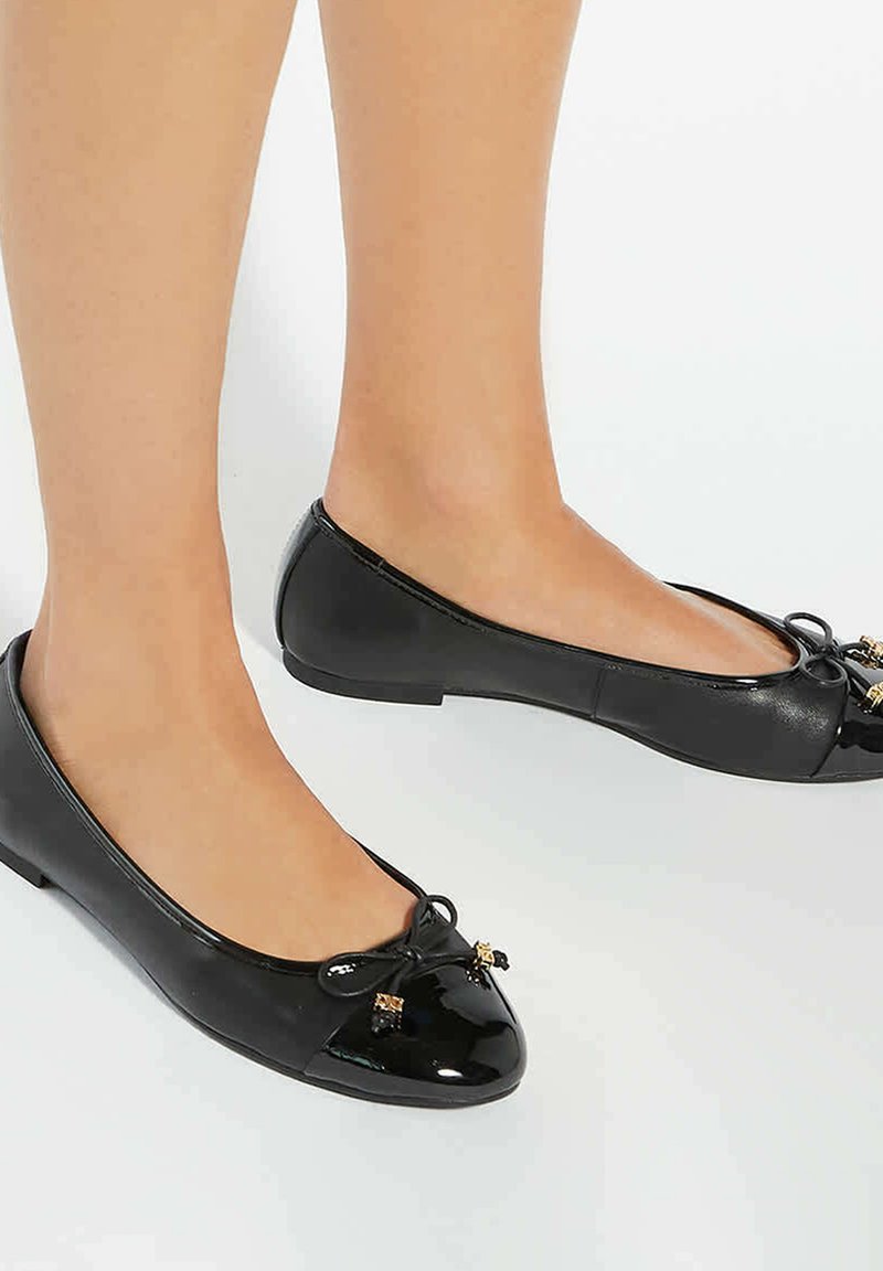 Zwarte lakleren ballerina's met een ronde neus, strikaccent en kleine gouden hardwaredetails. Platte zool en gladde textuur.
