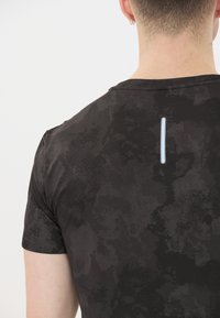 Mustat t-paita, jossa on teksturoitu kuvio, ja takana on hienovaraisia sinisiä yksityiskohtia. Lyhyet hihat ja pyöreä kaula-aukko.