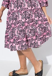 Pinke Leopardenmuster-Kleid mit gestuftem Saum, kurzen Ärmeln und relaxter Passform. Kombiniert mit schwarzen Sandalen mit Schnalle und Korksohle.