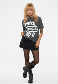 Gray graphic t-shirt with "oasis" design, paired with a black denim skirt and knee-high black boots. Smooth texture throughout.