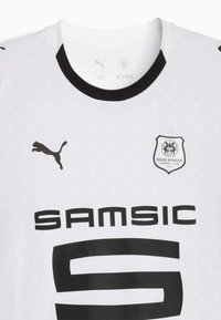 Camisa de fútbol blanca con acentos negros, que presenta un cuello negro, "SAMSIC" en letras grandes, el logo de Puma y el escudo del Stade Rennais.