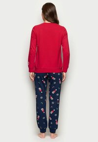 Punainen pitkähihaiset paita yhdistettynä tummansinisiin yöpaidan alaosiin, joissa on jännittäviä kuvioita, kuten joulupukin kasvoja, karkki keppijä ja lumihiutaleita.