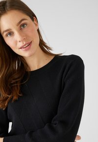 Suéter negro de punto con textura acanalada, con un escote redondo y un patrón diagonal en el frente. Mangas largas.