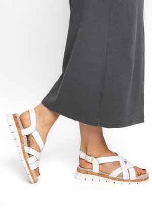 Feet wearing white leather sandals with cork soles and white buckles, paired with a dark gray skirt.