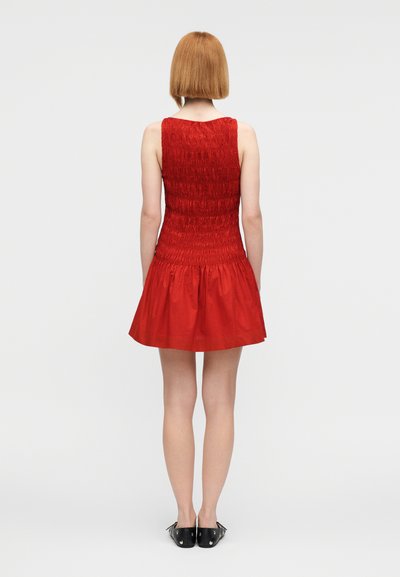 Κόκκινο αμάνικο φόρεμα με μέση σφηκοφωλιάς και φουσκωτή φούστα. Το ύφασμα έχει ομαλή υφή και το πίσω μέρος δείχνει ομοιόμορφη γραμμή τελειώματος.