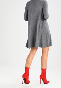 Robe en tricot gris avec un ourlet évasé, assortie à des escarpins à chaussette rouges vifs. La robe a des manches longues et une texture lisse.